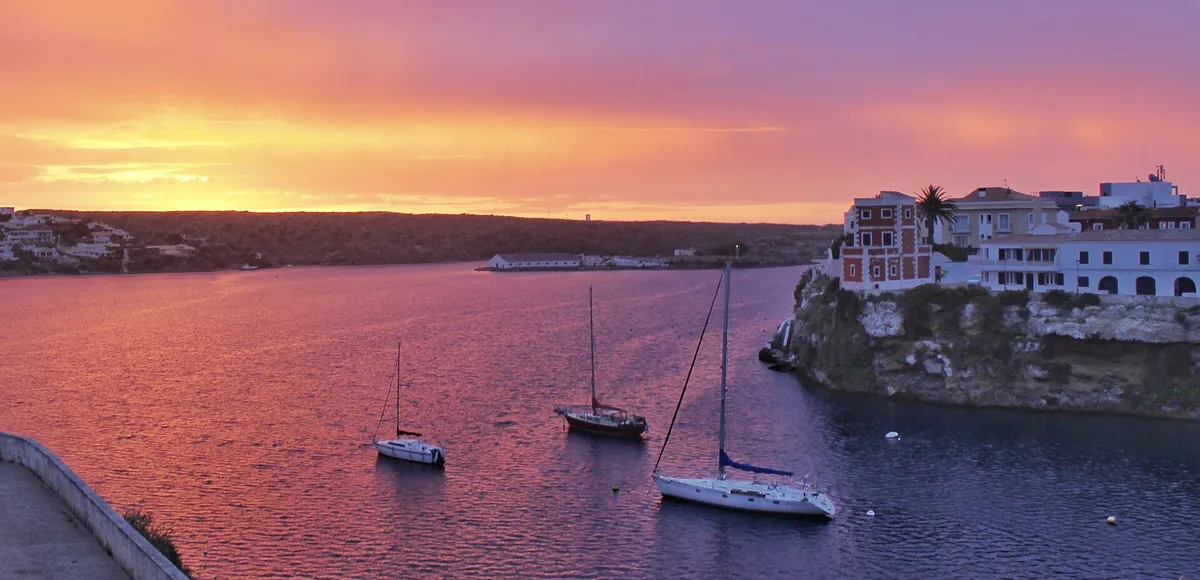 Fishing boats moored in calm water at sunrise in Cala Corb in Es Castell near Mahon, Menorca