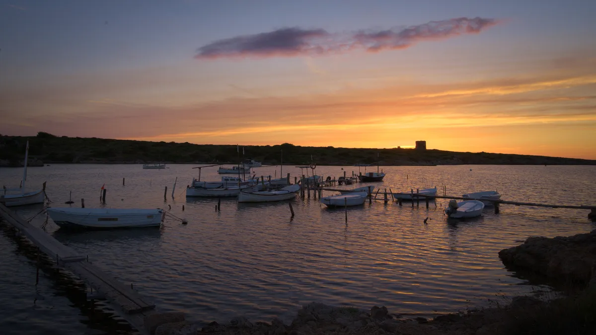 Sunset over small boats at anchor by the Cap de Cavalleria headland on the north coast of Menorca