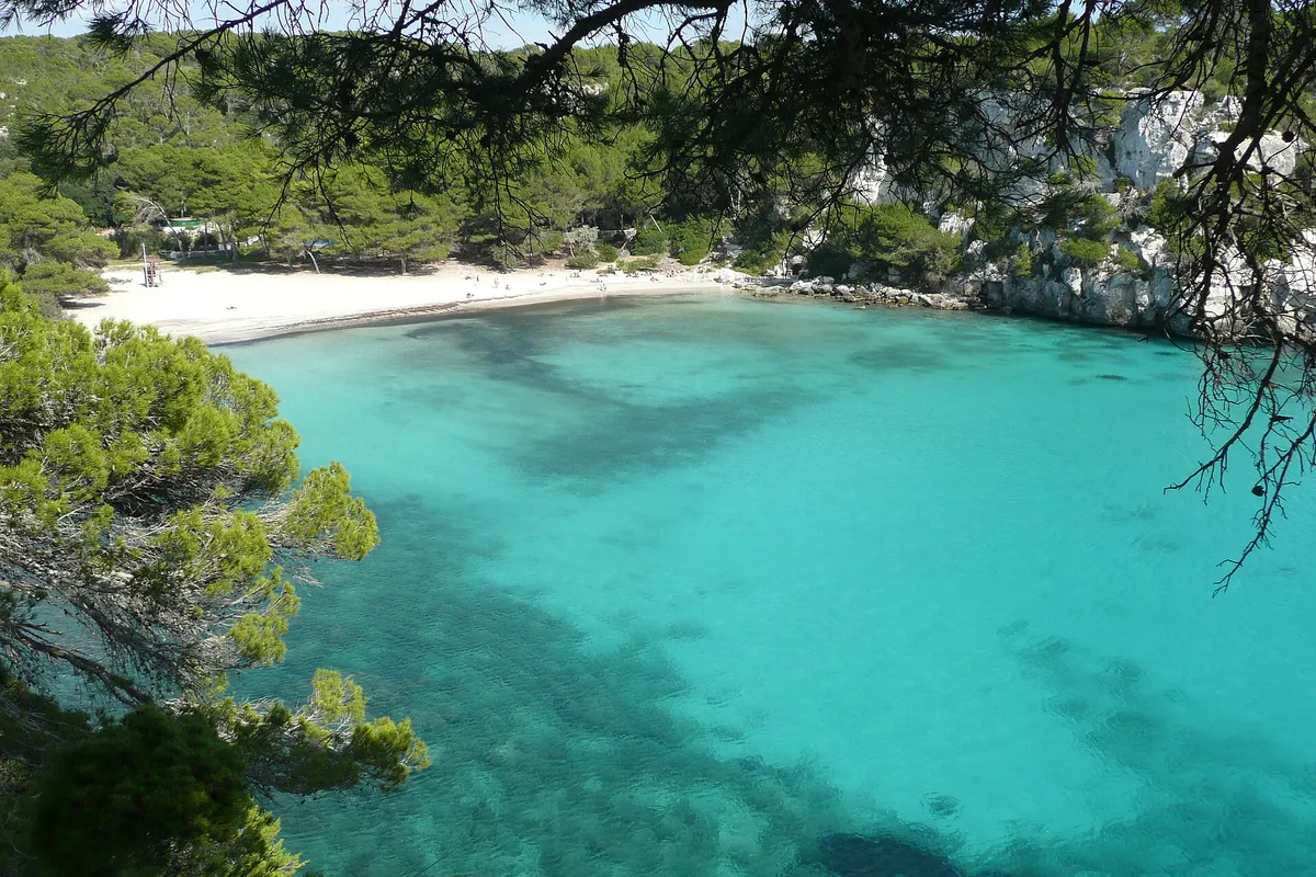 White sand and turquoise water at Cala Macarella in Menorca, the kind of cove a boat trip reaches at its best in June or September