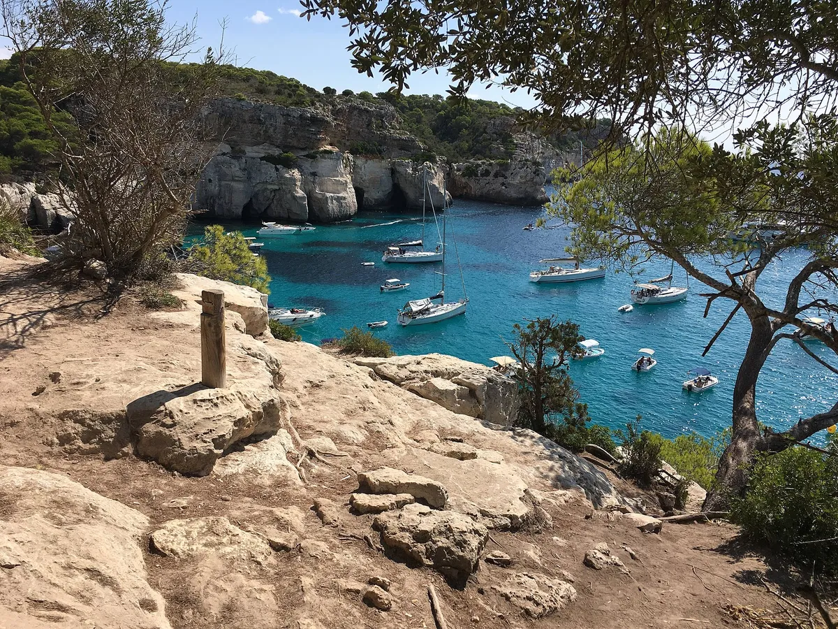 The Cami de Cavalls coastal path above Cala Macarella in Menorca with boats at anchor seen from the walking route