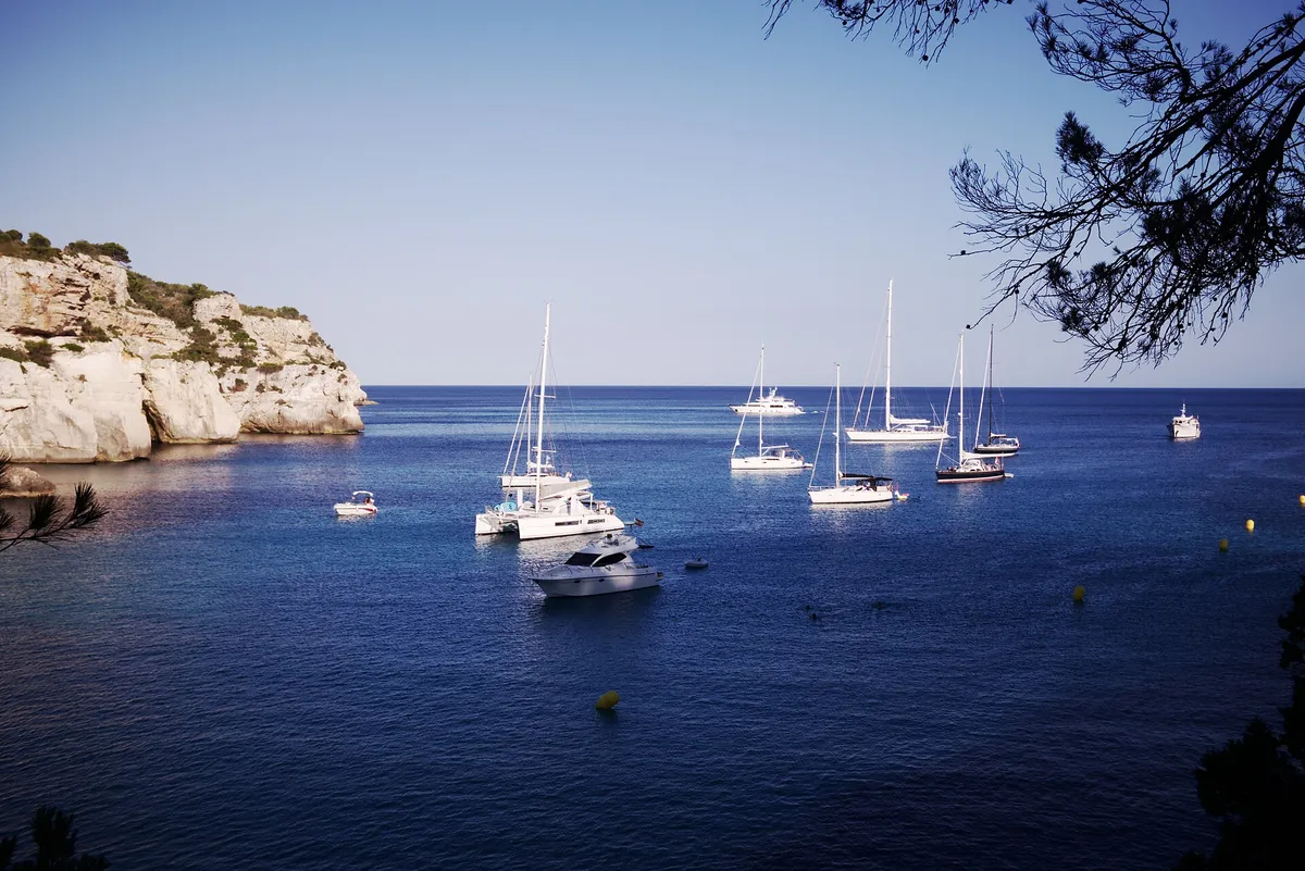 Sailing boats anchored off the white cliffs near Cala Macarella in Menorca, seen from the seaward approach