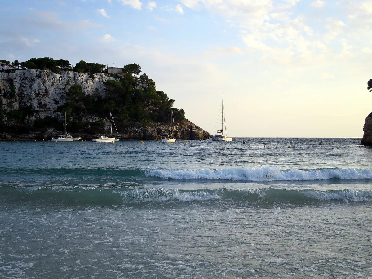 Calm turquoise water and boats in Cala Galdana bay in Menorca, the departure point of the island's most family-booked boat trips with kids